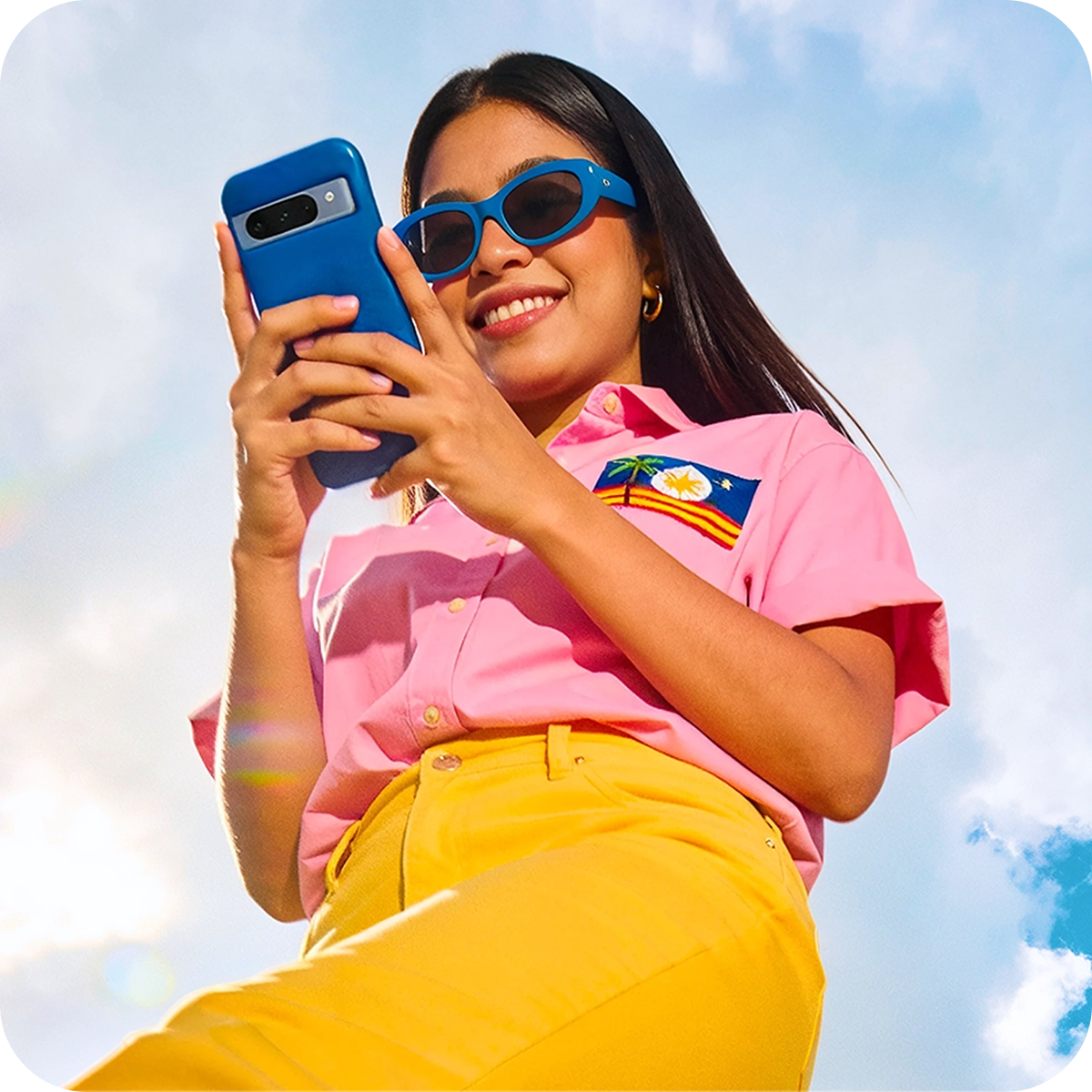 a young woman wearing a pink shirt and yellow sunglasses holding a blue phone