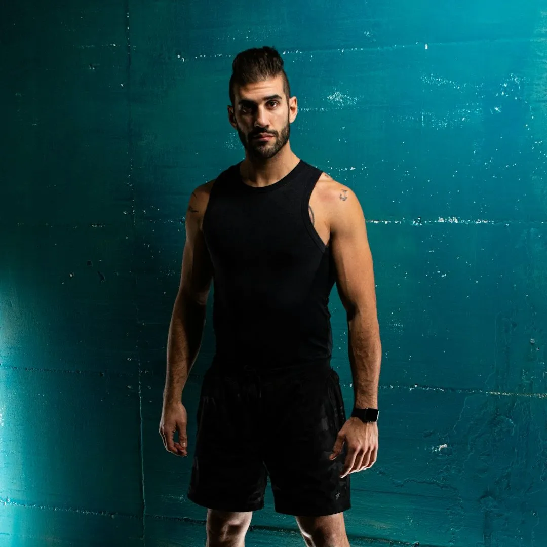 man in black tank top and shorts standing beside blue wall