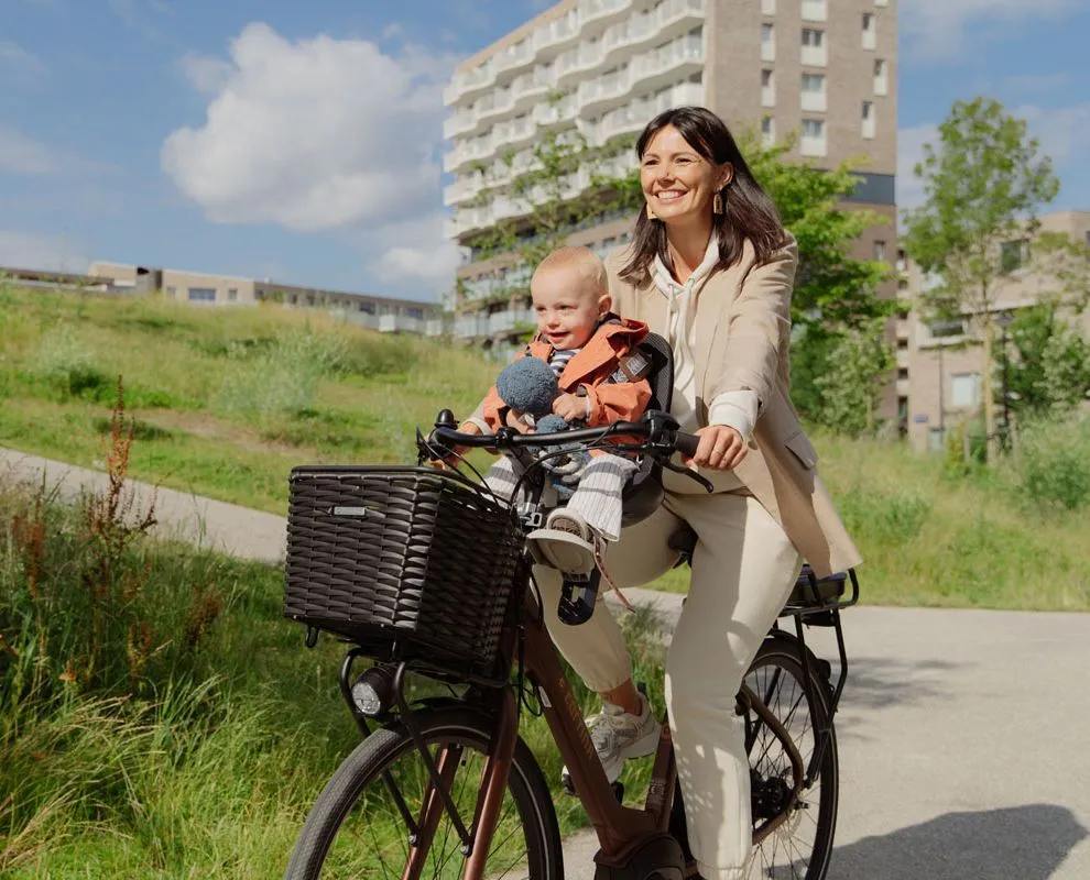 vrouw fietsend op een cortina e-common family familiefiets met een mandje en kinderzitje voorop