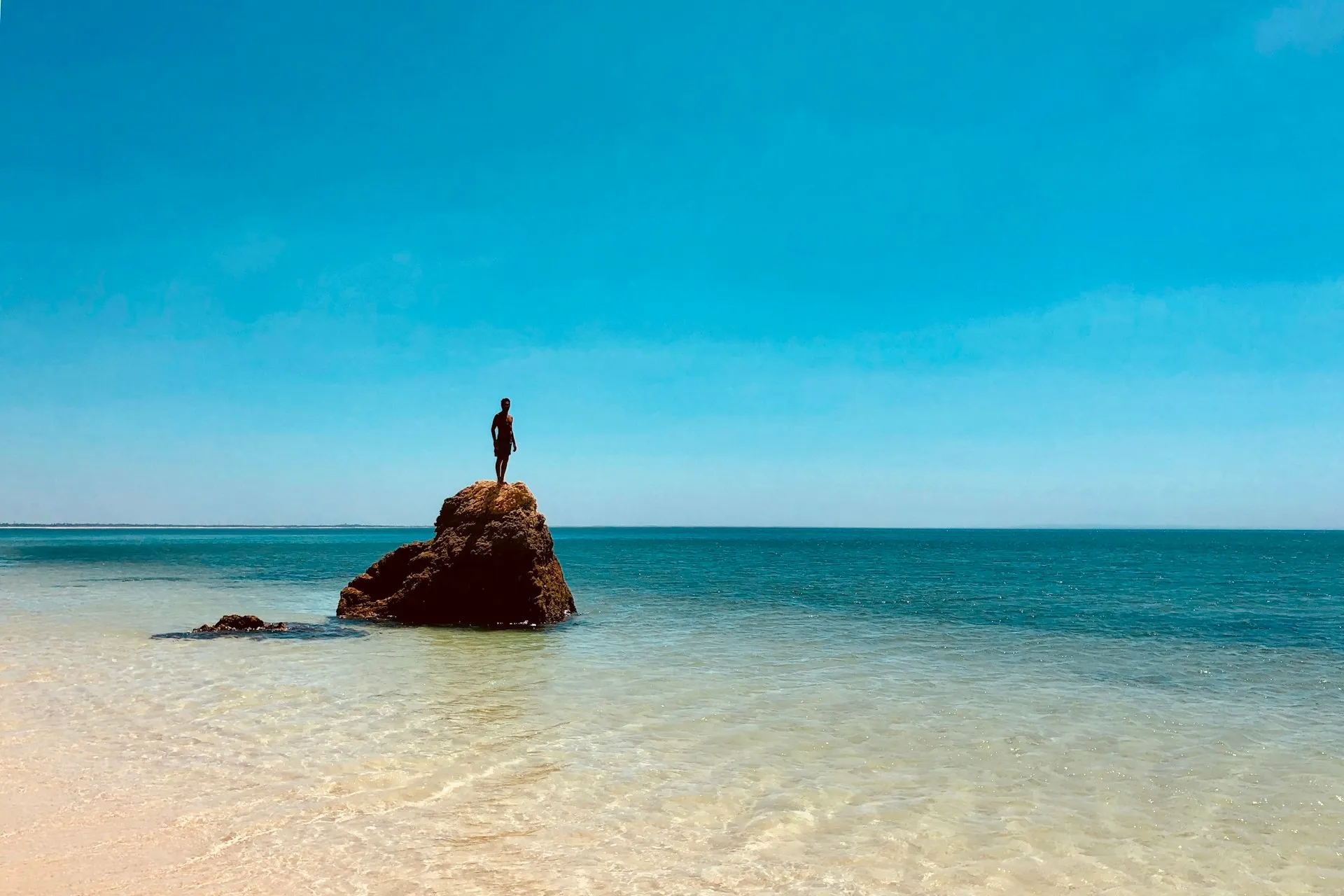 person standing on top of rock across sea during daytime