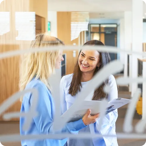 Zwei Mitarbeiterinnen lächelnd während sie eine Produktinformationsbroschüre in der Hand halten