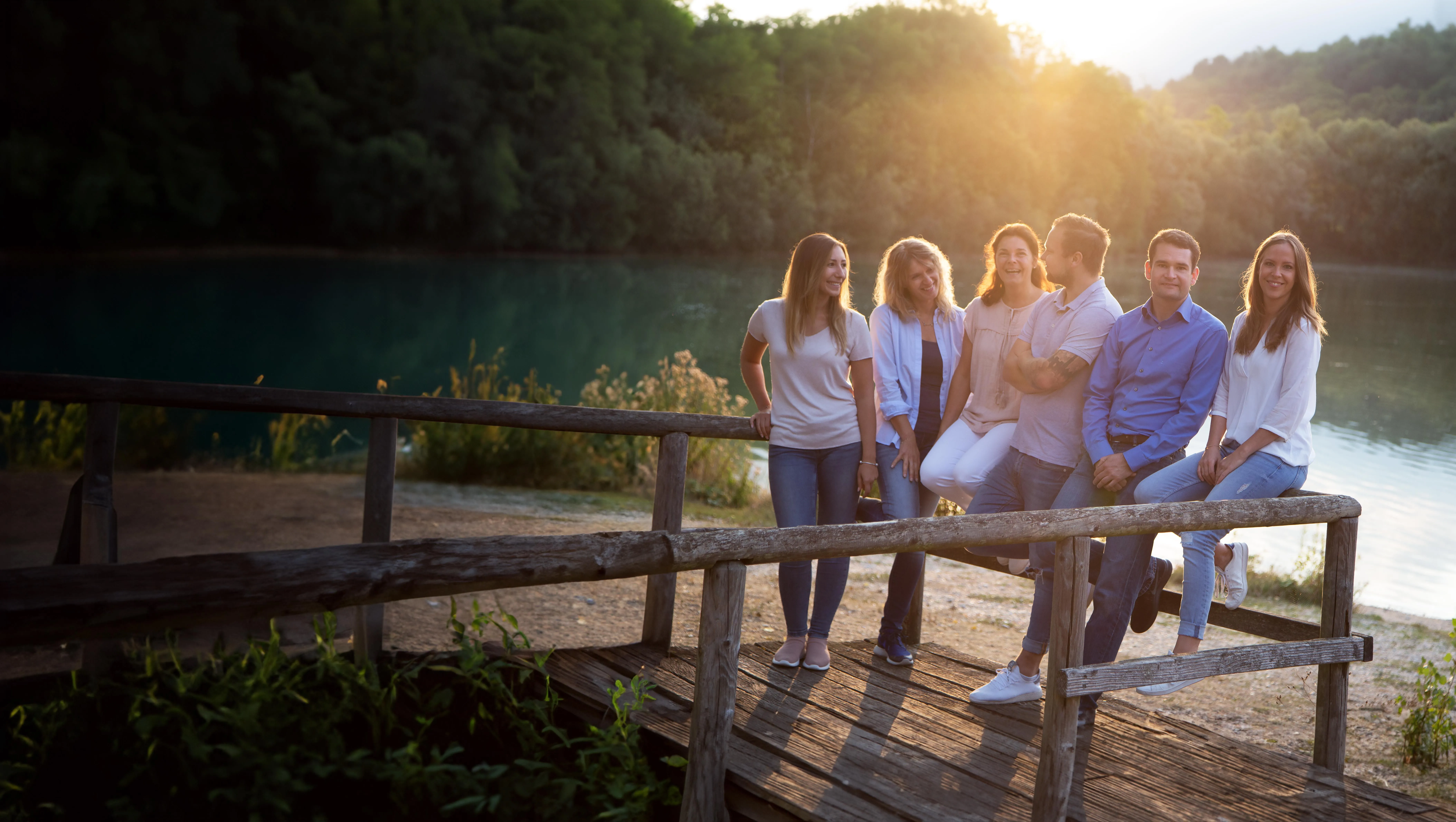 Gruppe von erwachsenen Personen steht lächelnd vor See bei Sonnenaufgang